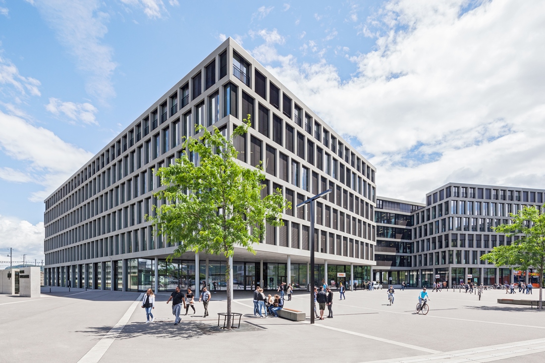  Auf dem Foto ist der Campus Brugg-Windisch. 
Es sind mehrere Gebäude.
Die Gebäude sind modern.
Menschen sind auf dem Platz vor dem Campus. 